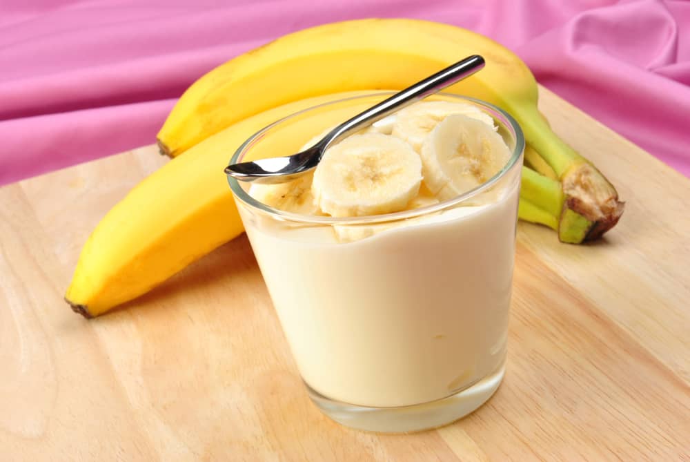 Curd in the glass with some banana pieces on the top  while banana is at back of the glass