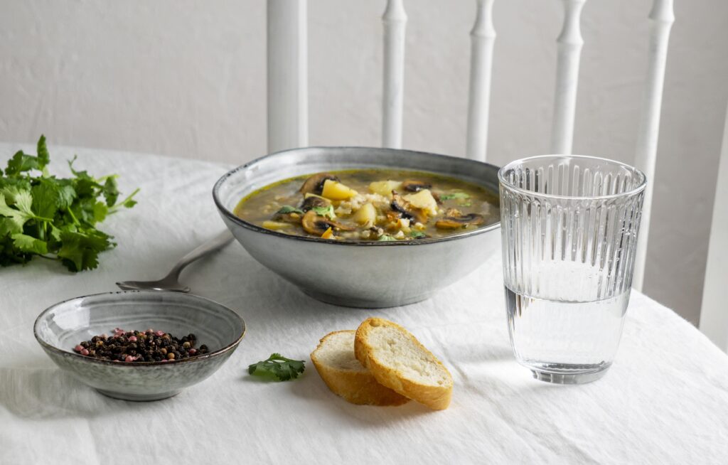 Some bowls of brothe bone, beans with a glass of water and bread are kept on table 